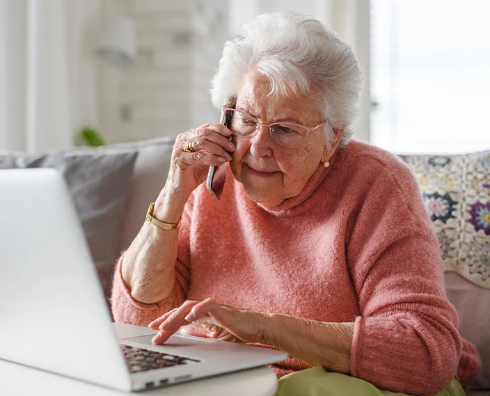 Older woman calling on phone for support while browsing on laptop