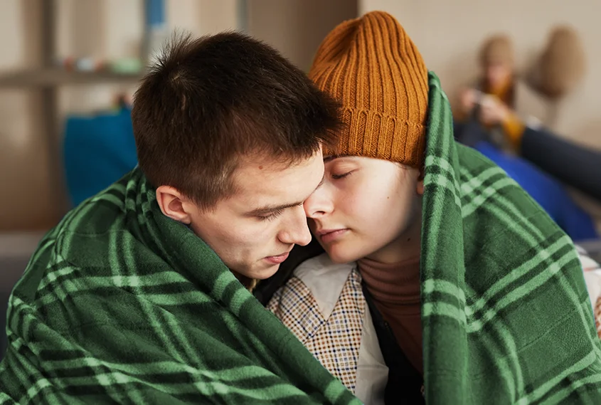 Homeless people huddled in a blanket indoors